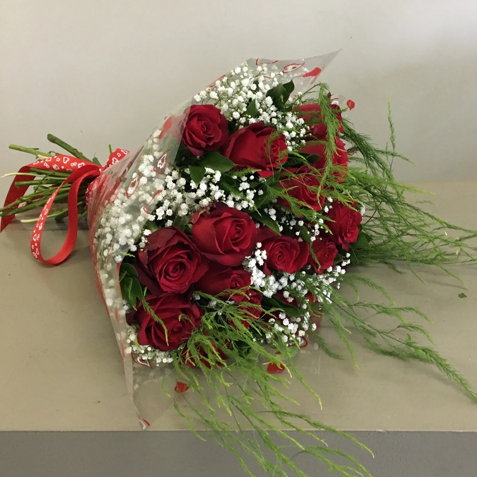 Hand-tied bunch of red roses with gypsophila and fern in heart-print cellophane