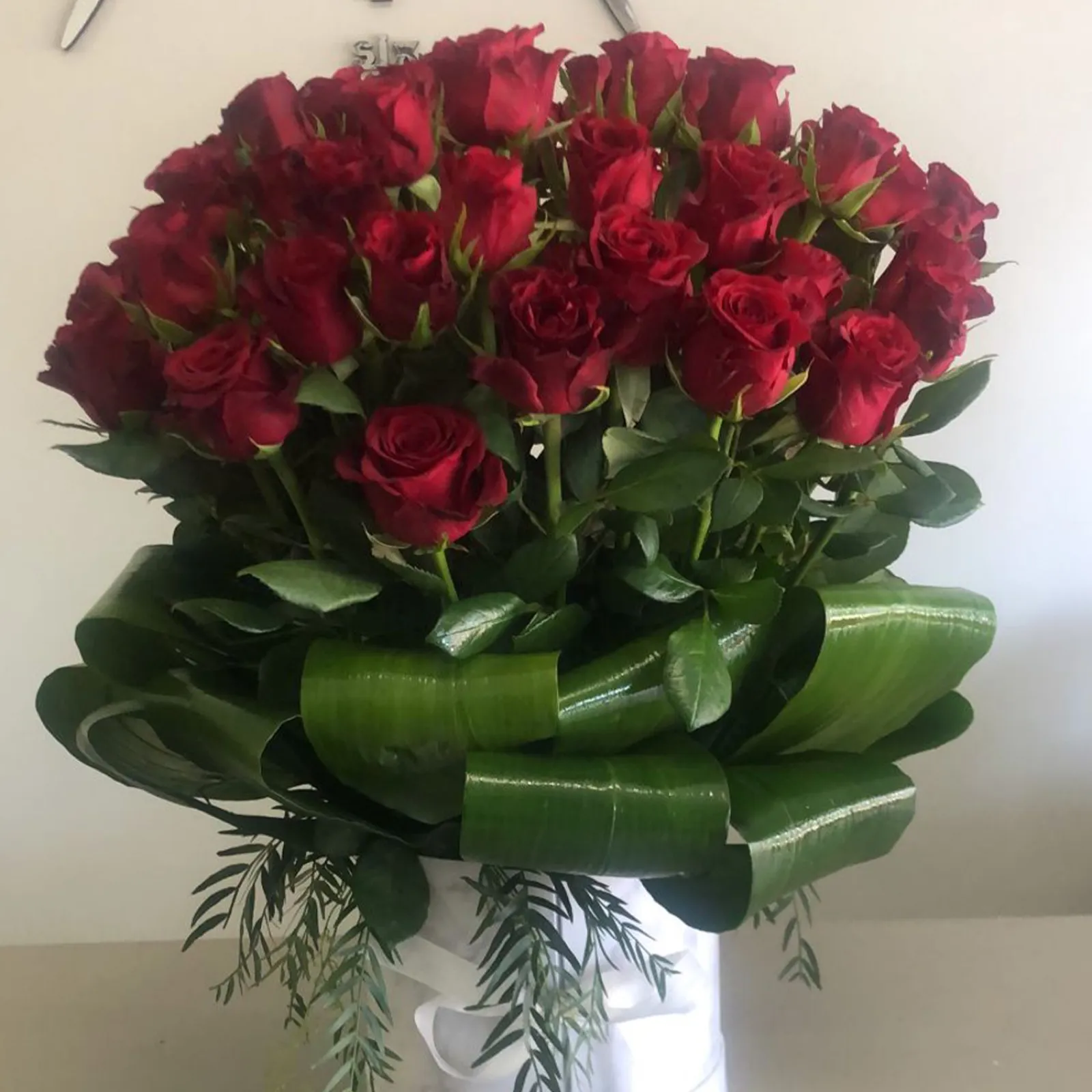 Fifty red roses collared with rolled green leaves in a white hat box