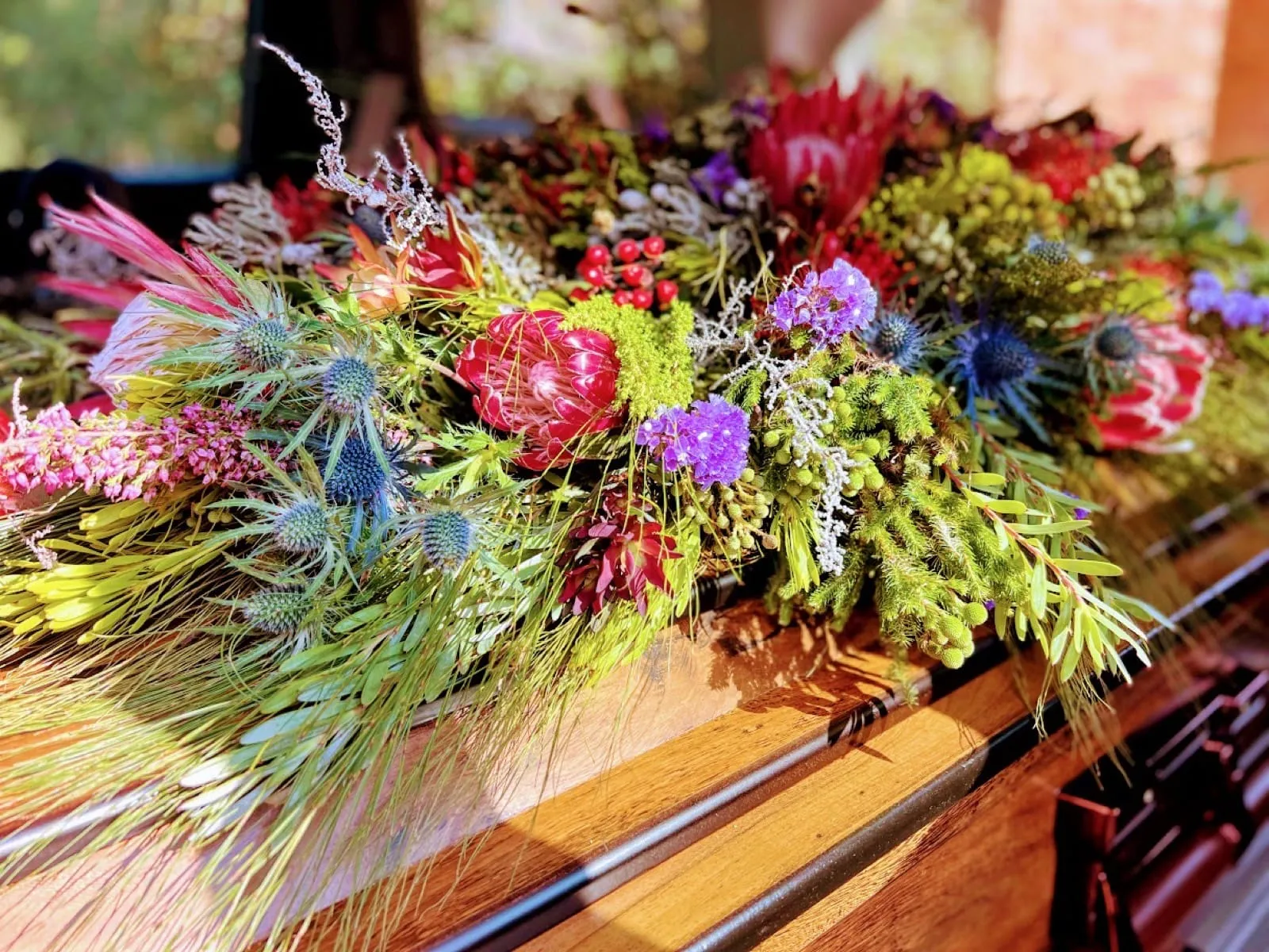 Natural casket spray of proteas, pincushions, blue thistles and fynbos on a wooden coffin