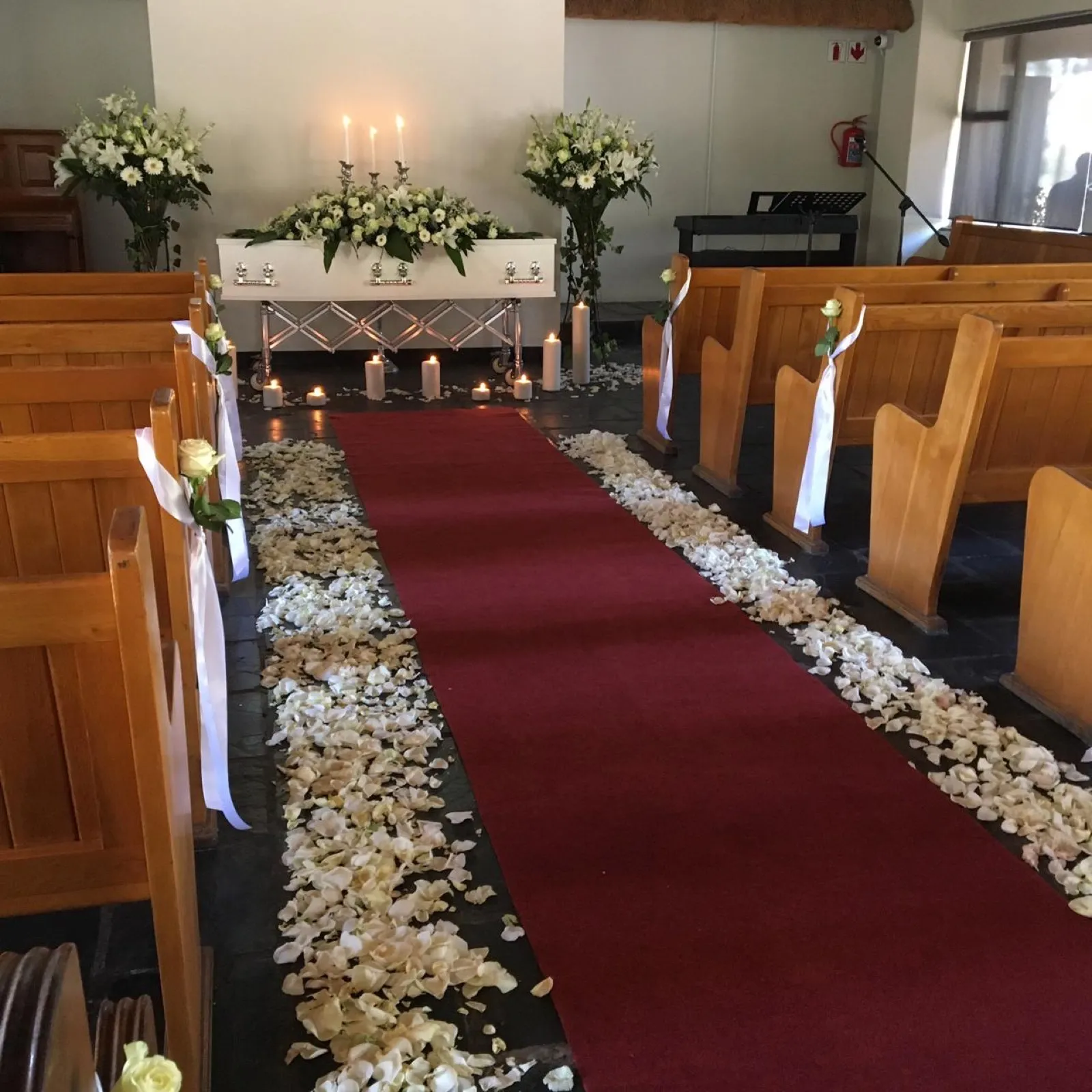 Chapel aisle lined with white rose petals leading to a coffin with a white spray