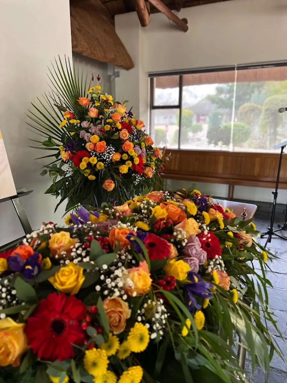 Bright casket spray on a coffin with a matching tall pedestal arrangement in a chapel