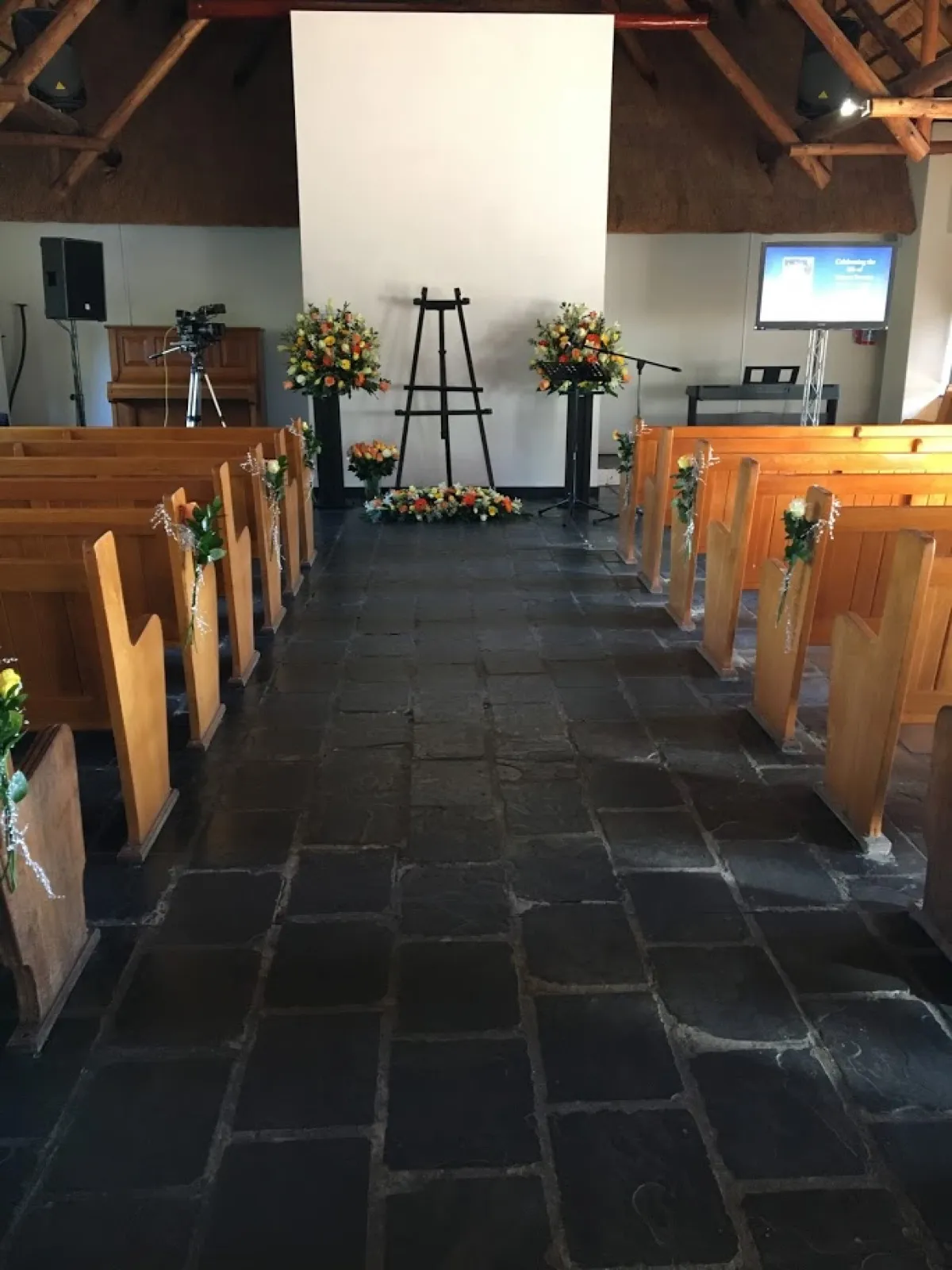 Chapel aisle with pew posies, two pedestal arrangements and a floor spray by an easel
