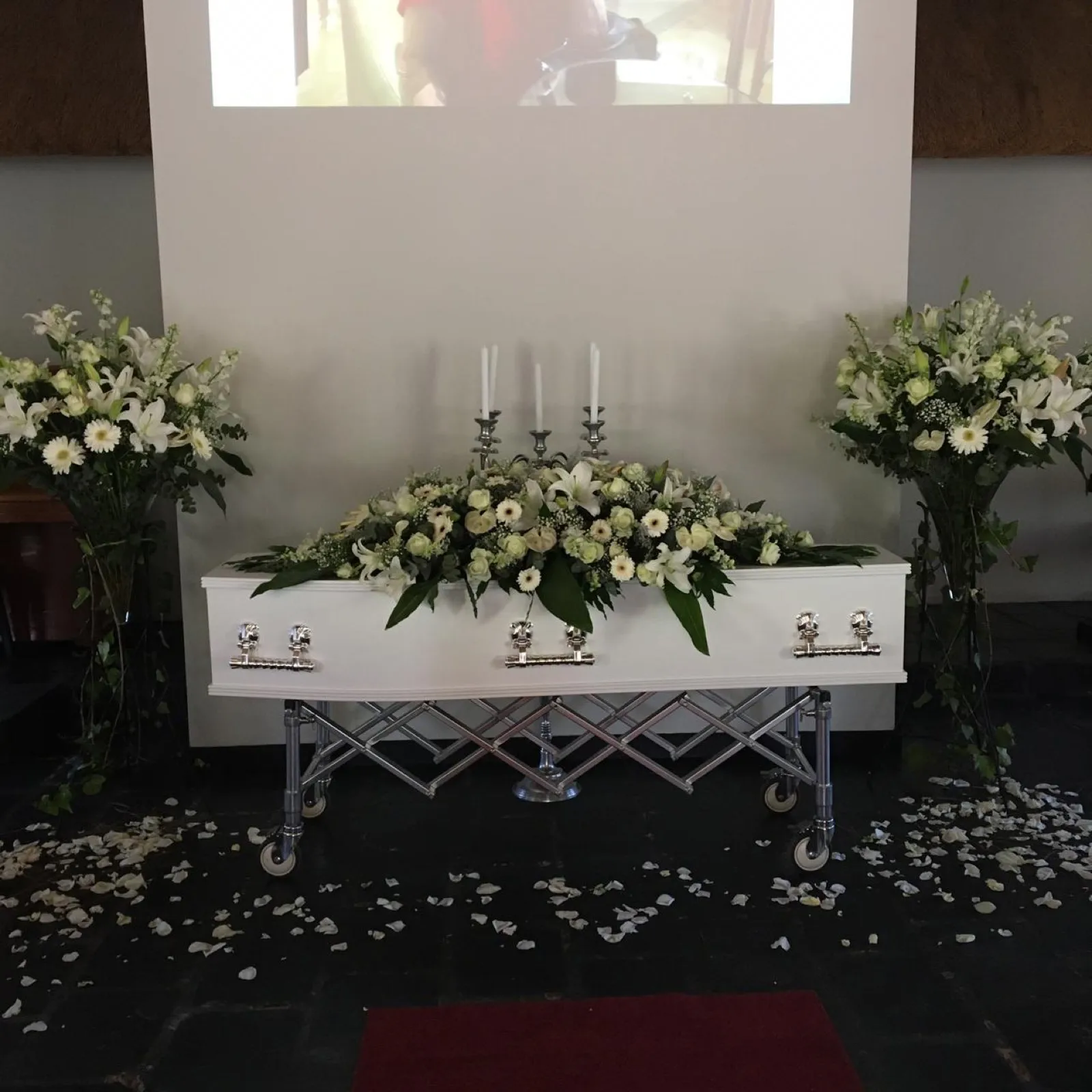 White casket spray on a white coffin flanked by two tall vases of white lilies