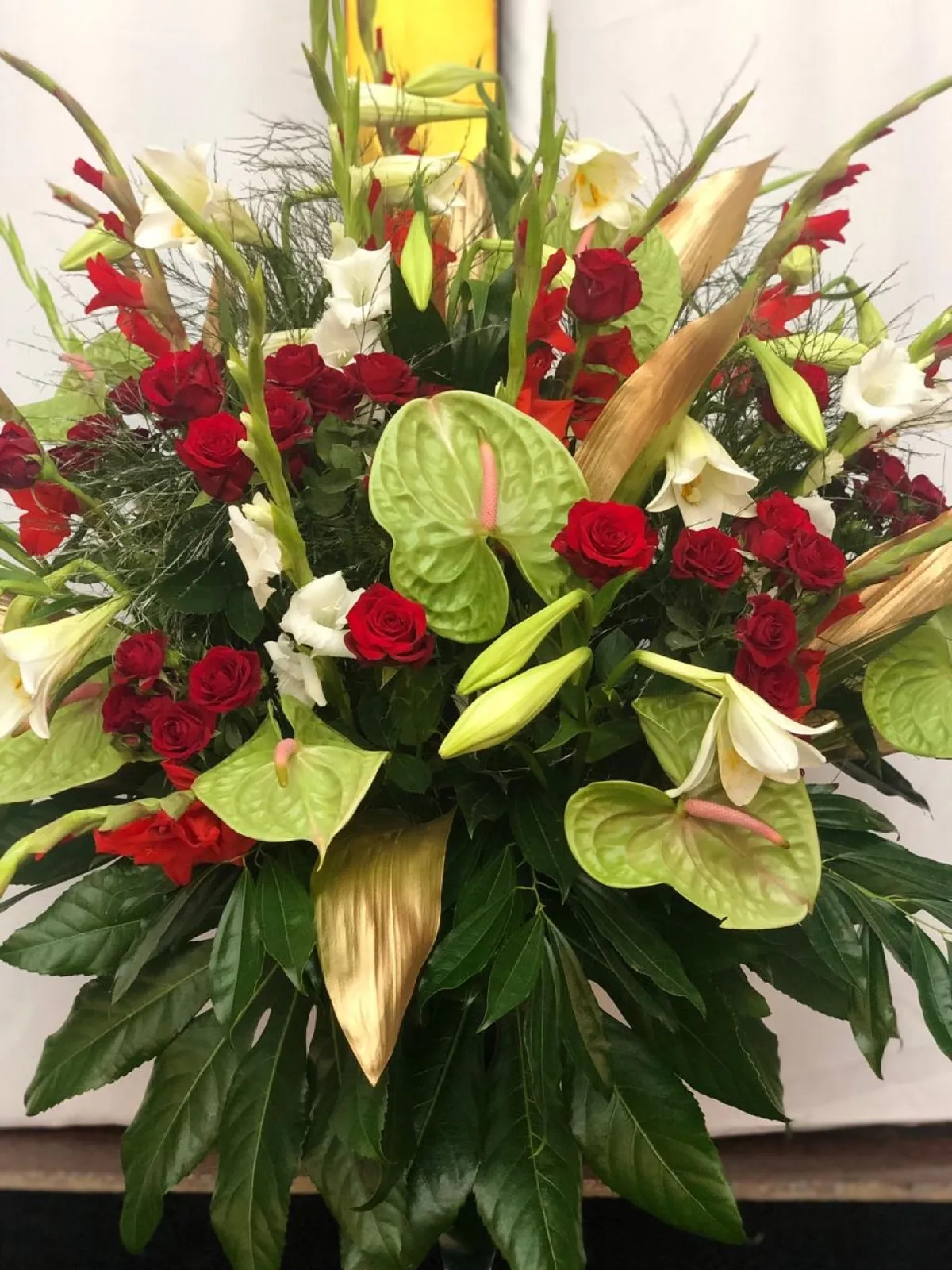 Christmas church arrangement of red roses, green anthuriums, white lilies and gold leaves