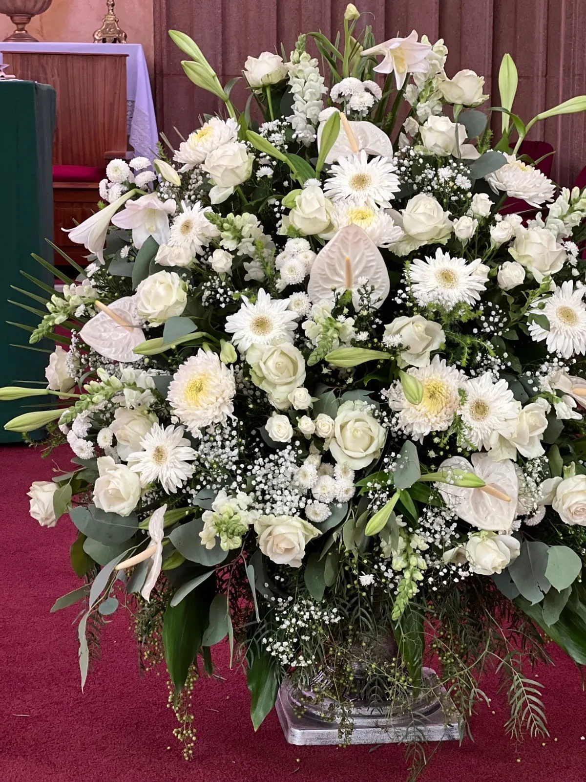 Large all-white church arrangement of roses, gerberas, lilies and anthuriums on a pedestal