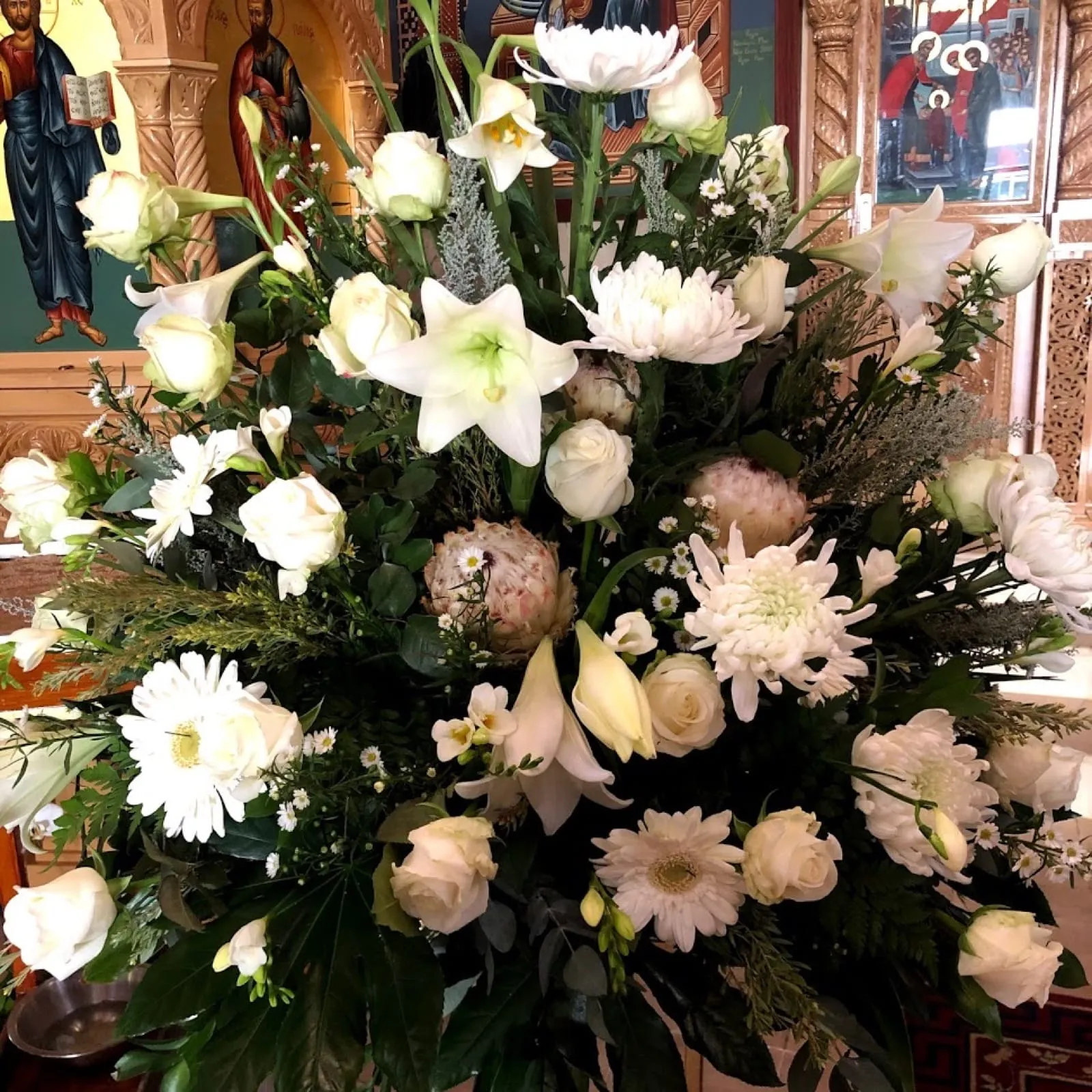 White church arrangement of roses, lilies and chrysanthemums in front of Orthodox icons