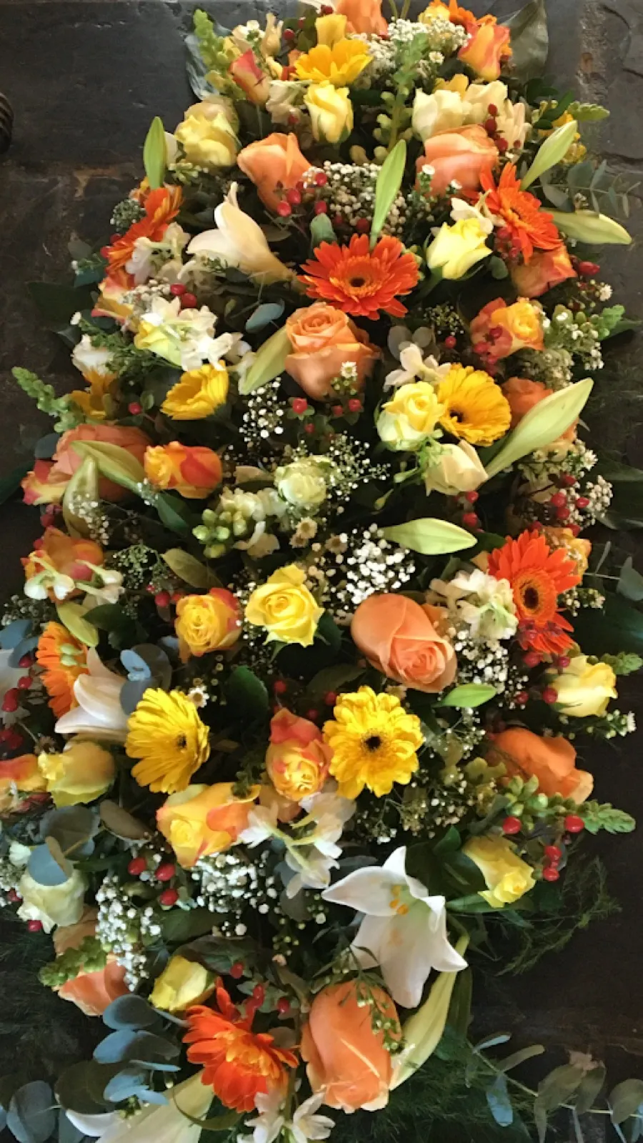 Long casket spray of yellow and peach roses, orange gerberas and white lilies