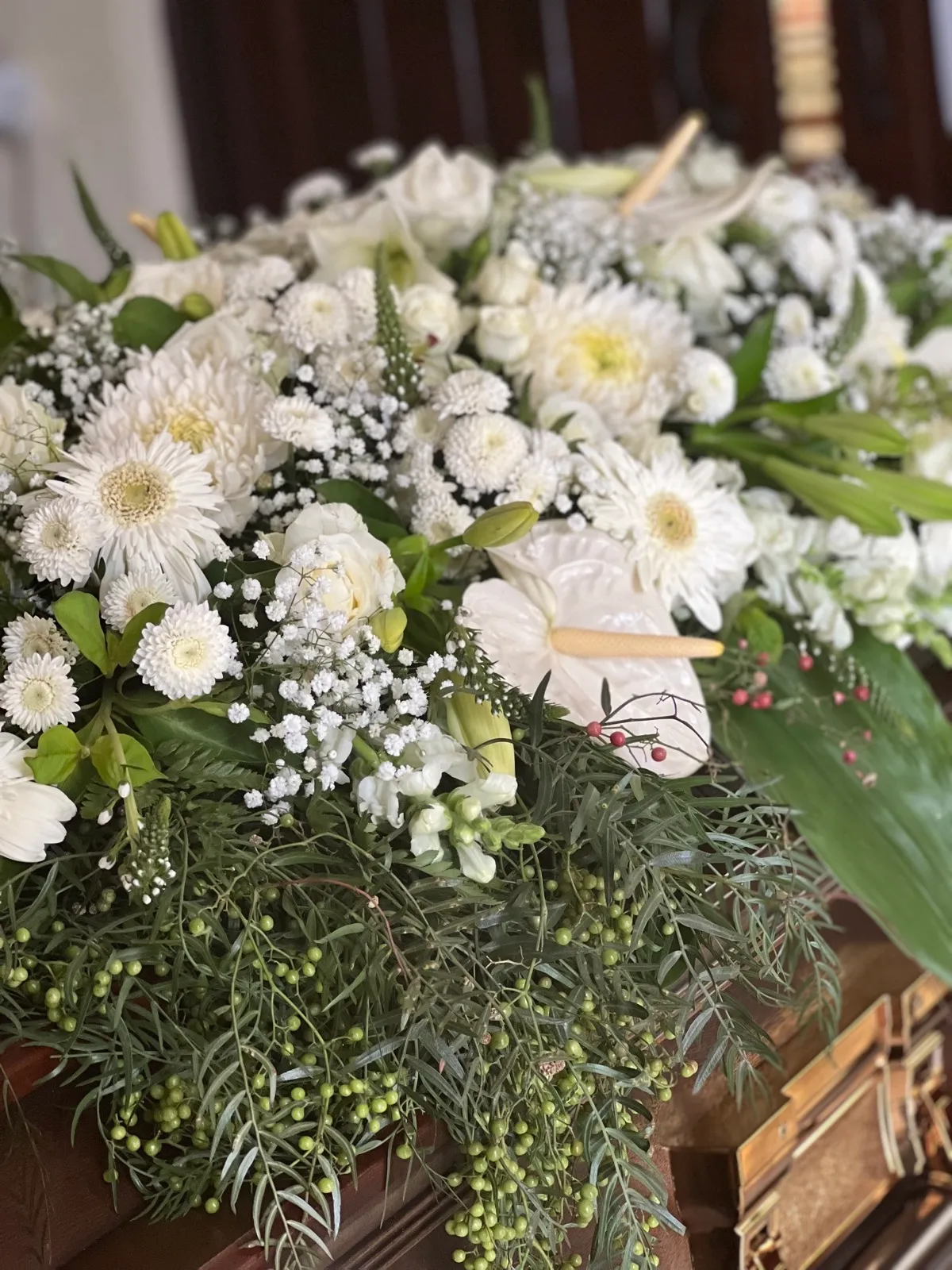 White casket spray of gerberas, chrysanthemums, anthuriums and roses with pepper berries