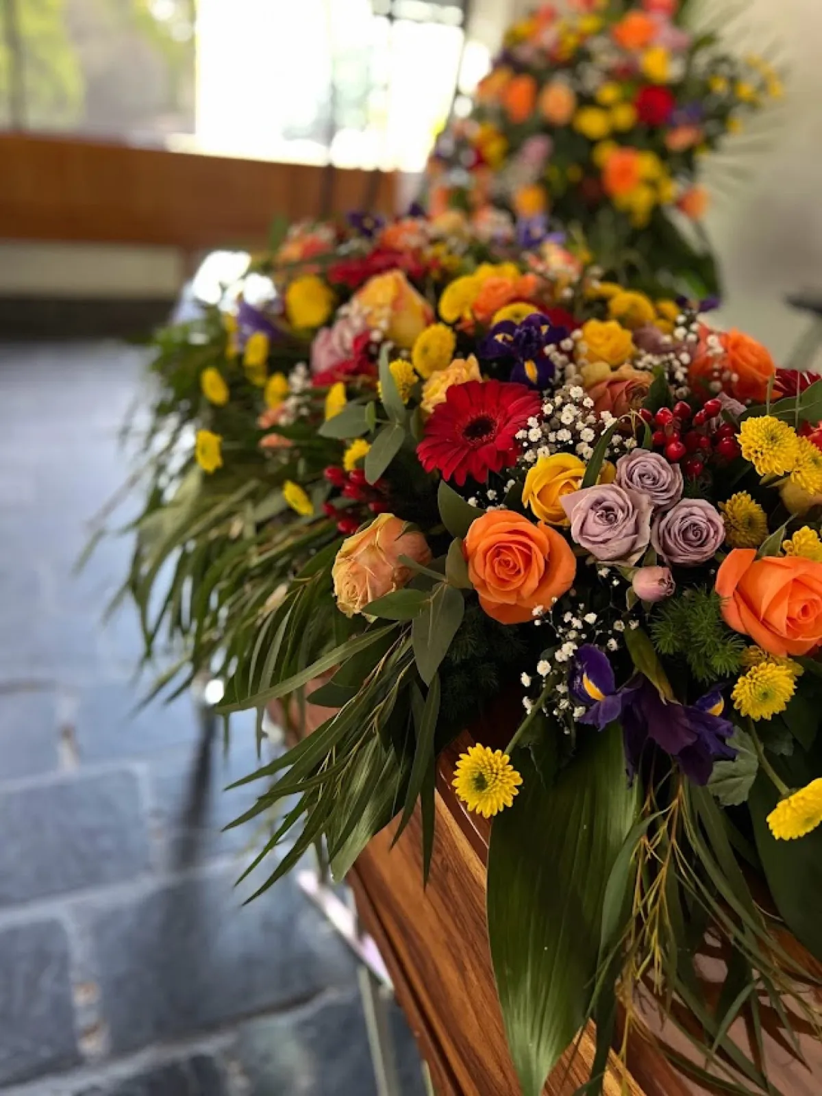Colourful casket spray of orange roses, yellow and red gerberas and irises on a wooden coffin