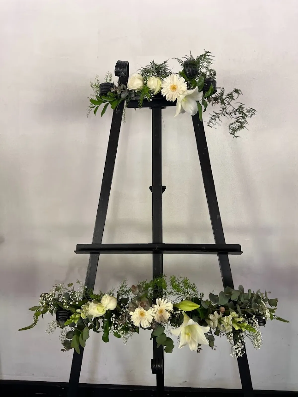 Black display easel decorated with two garlands of white roses, gerberas and lilies