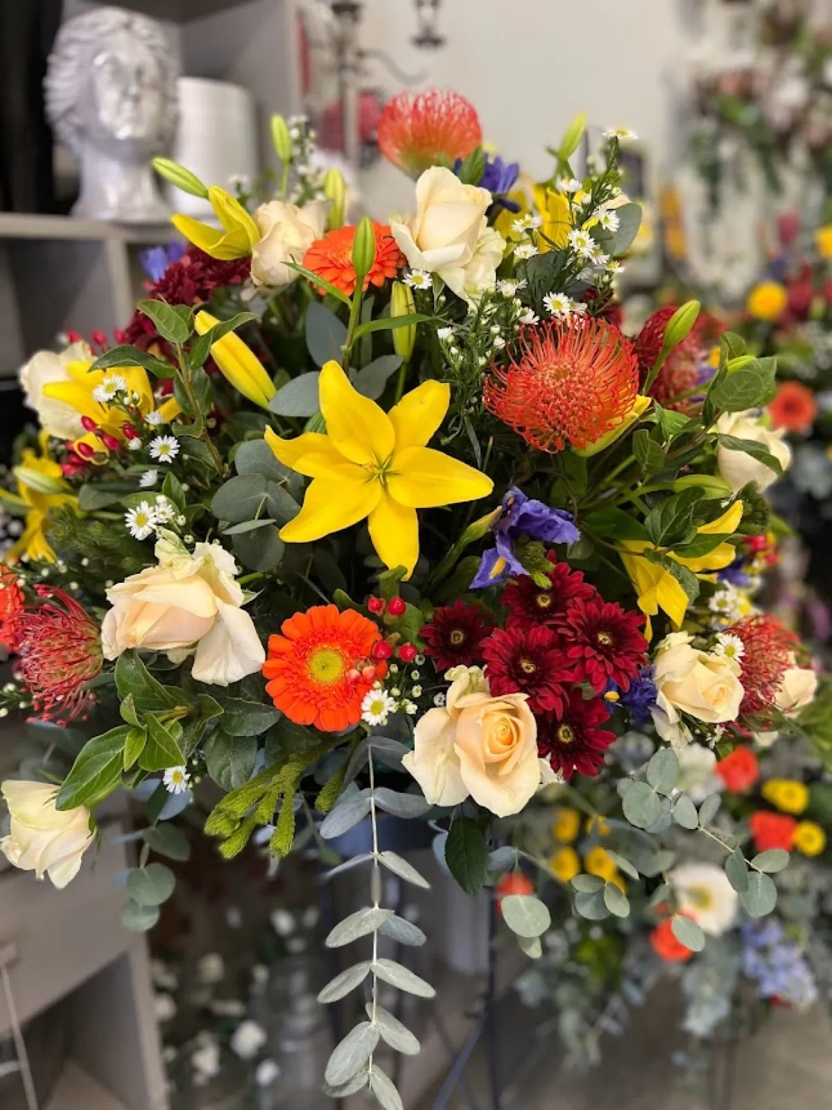 Bright mixed arrangement of yellow lilies, cream roses, orange pincushions and gerberas