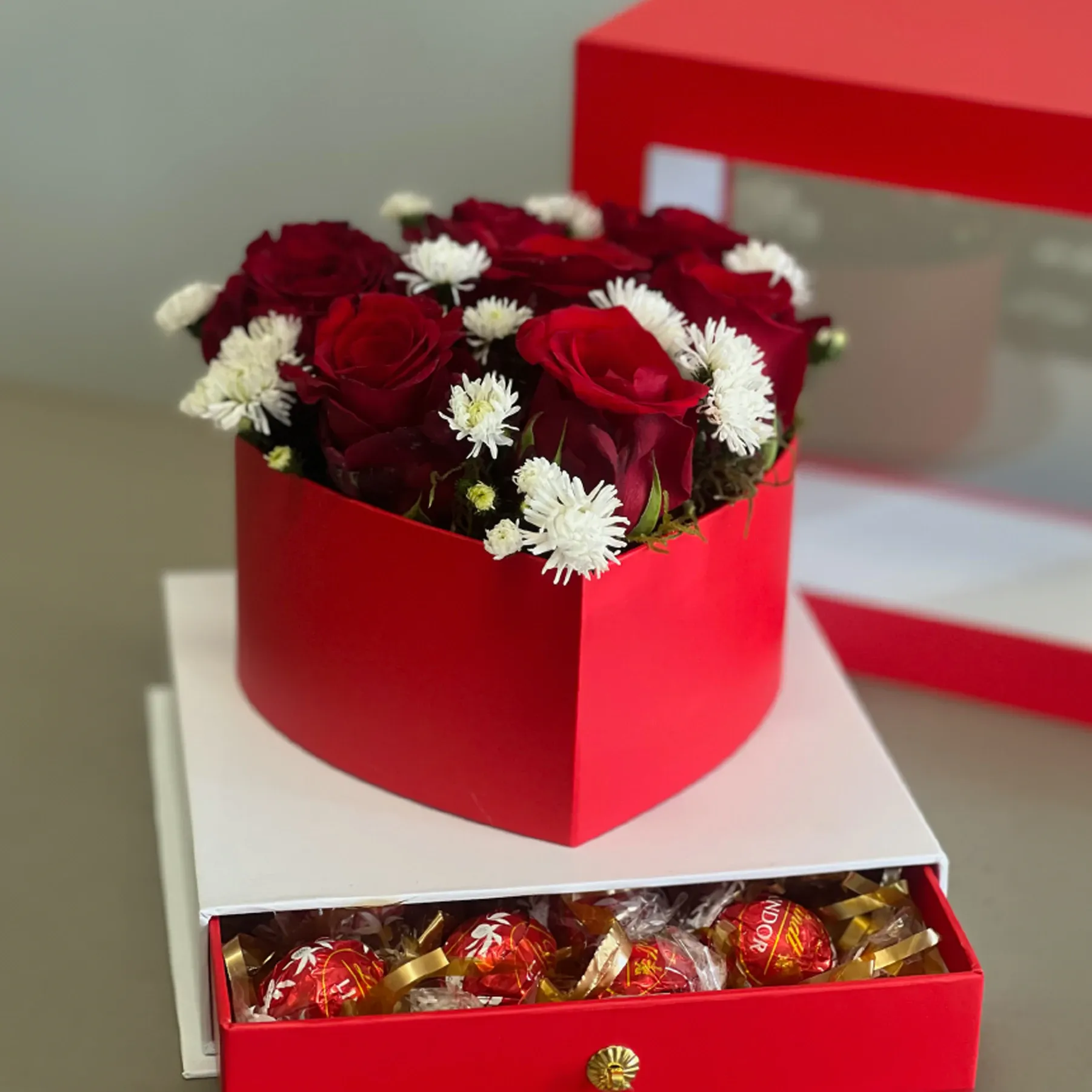 Red heart box of red roses and white daisies on a drawer of Lindor chocolates