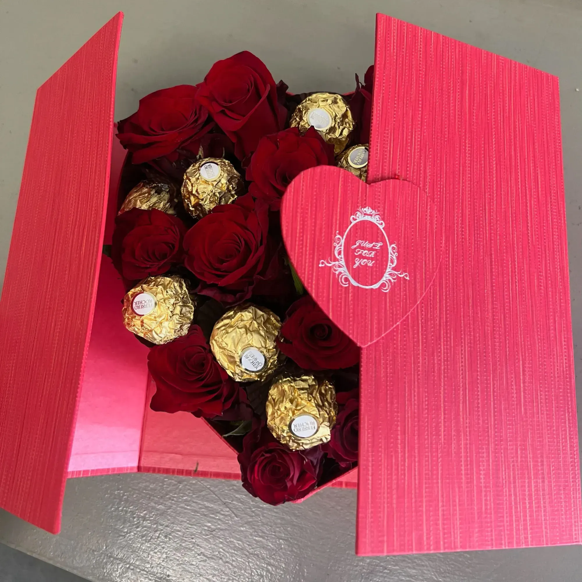 Open red gift box with red roses, Ferrero Rocher chocolates and an 'I love you' heart lid
