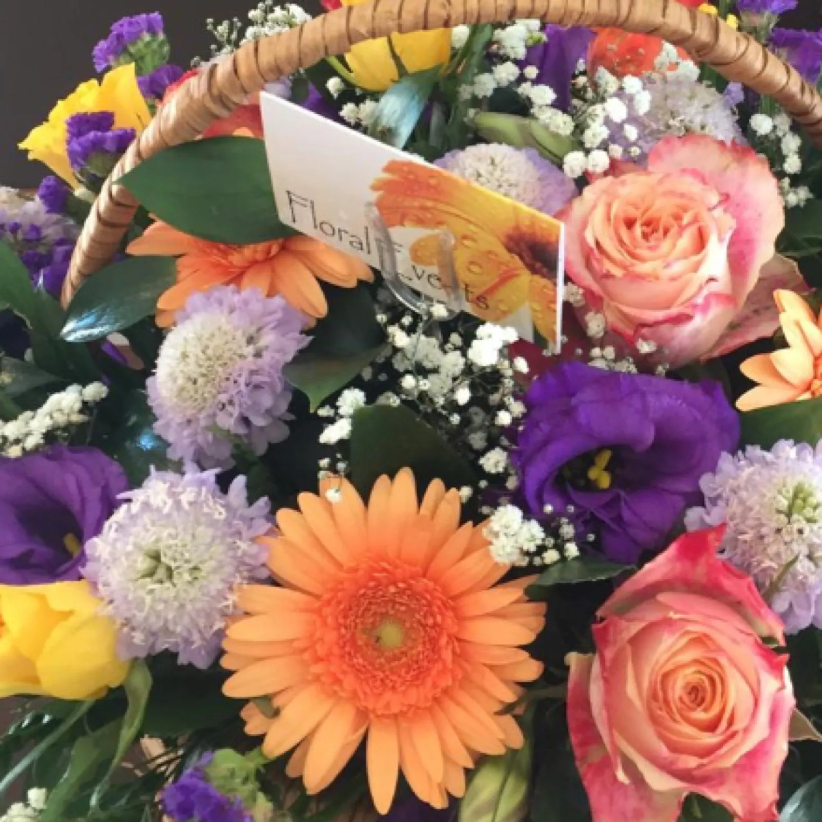 Wicker basket of orange gerberas, peach roses, purple lisianthus and lilac scabiosa