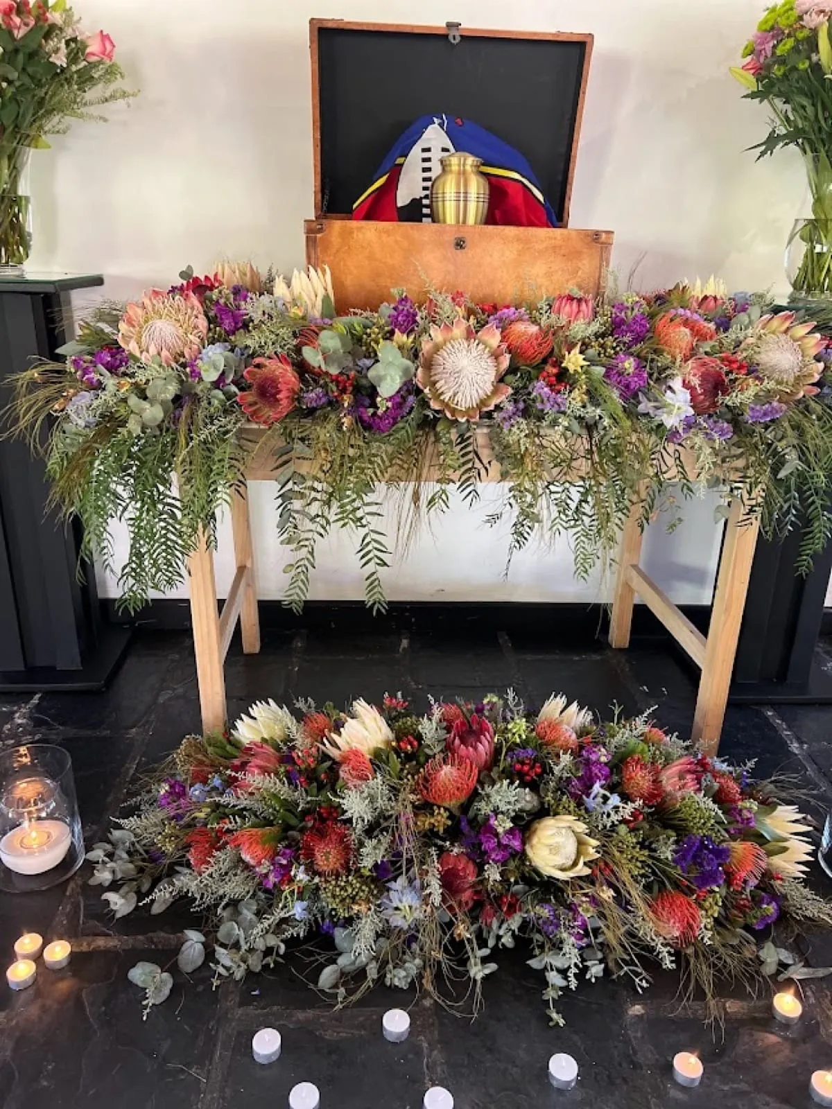 Protea, pincushion and fynbos spray on a memorial table with an urn, plus a matching floor spray