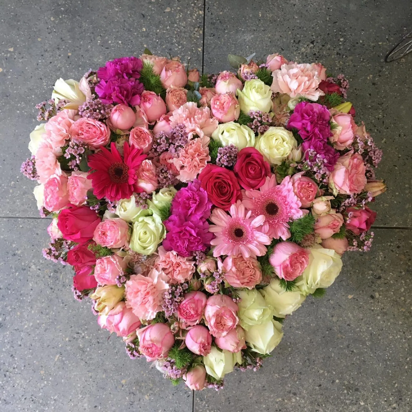 Heart-shaped tribute of pink roses, carnations and gerberas laid on a tiled floor