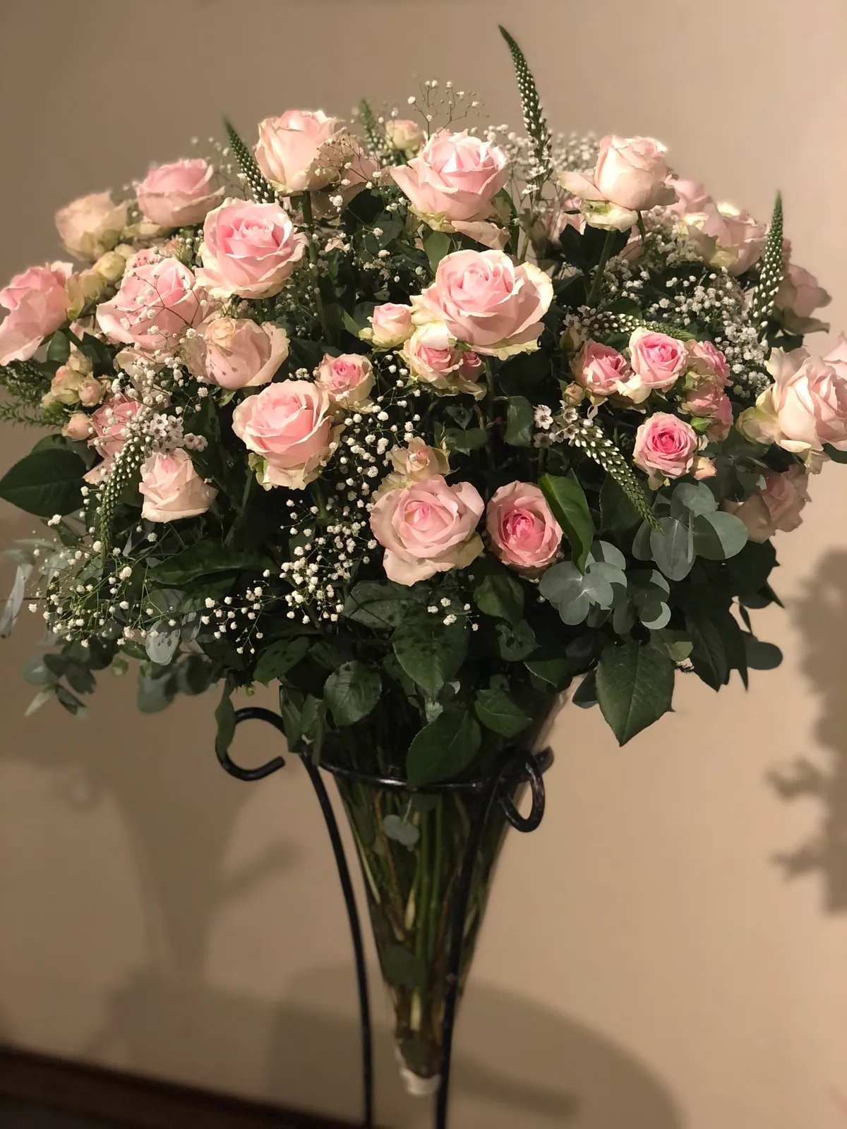 Soft pink roses with gypsophila and eucalyptus in a tall glass cone vase on a stand