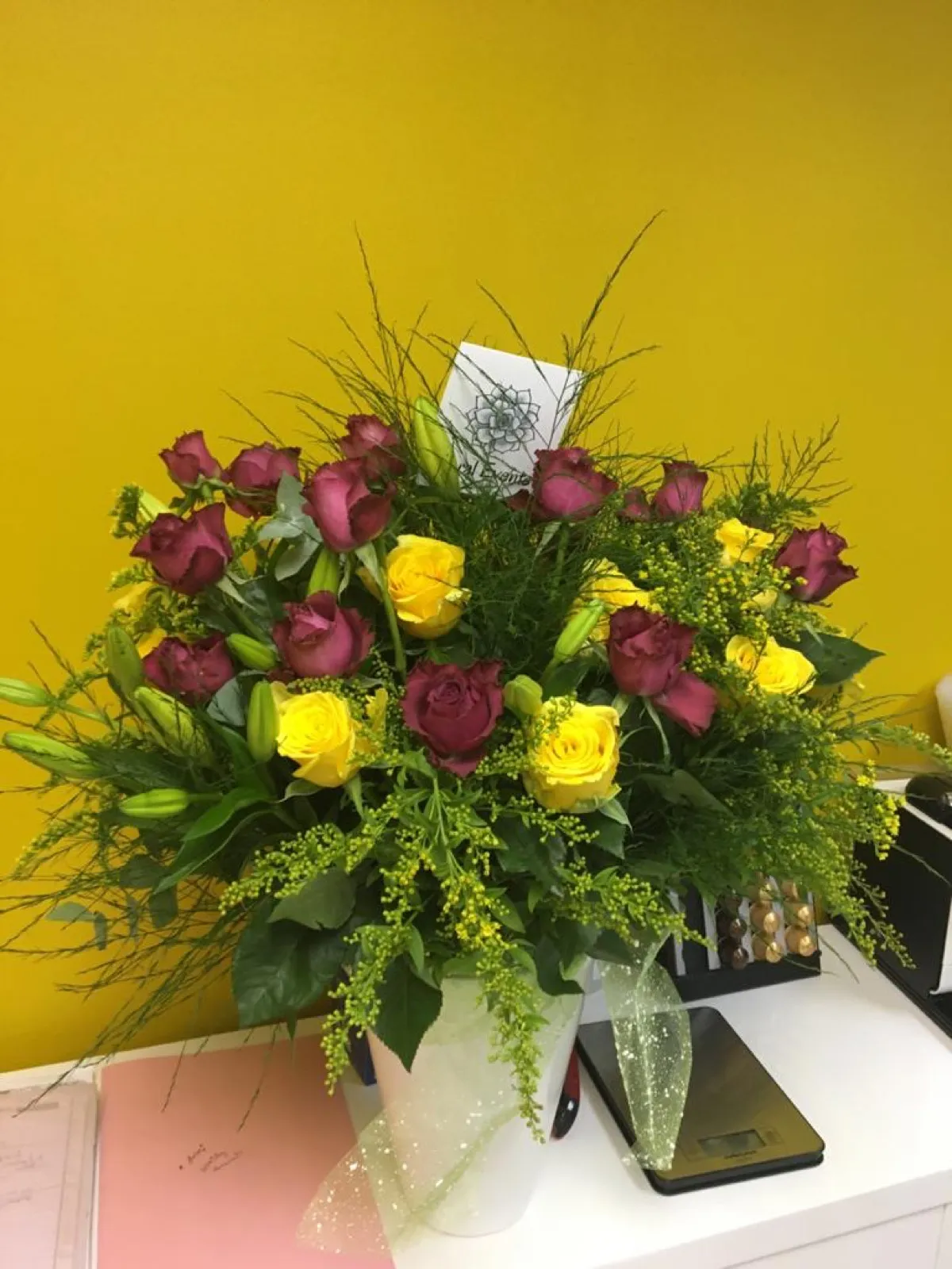 Deep purple and yellow roses with solidago in a white ceramic vase