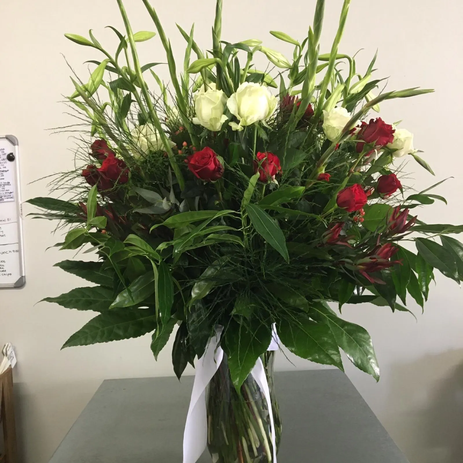 Tall glass vase of red and white roses with gladioli and glossy greenery