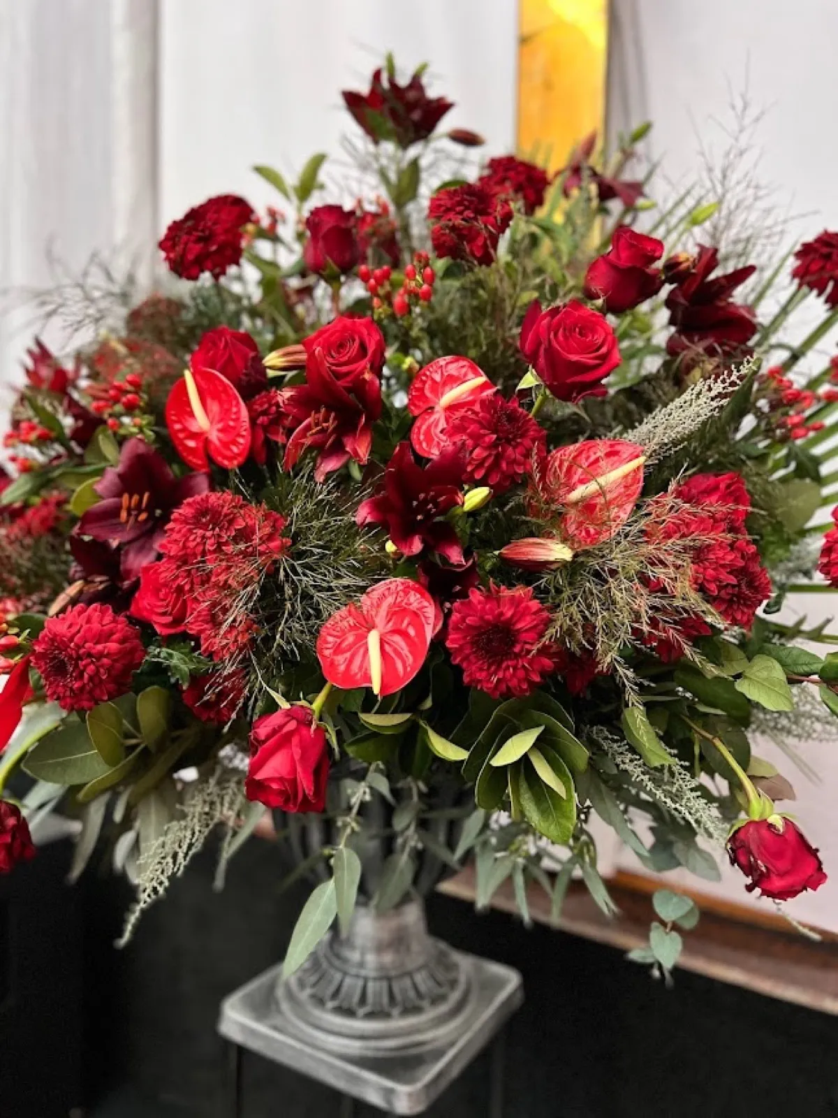 Large red church arrangement of roses, anthuriums and lilies in a pewter urn on a pedestal