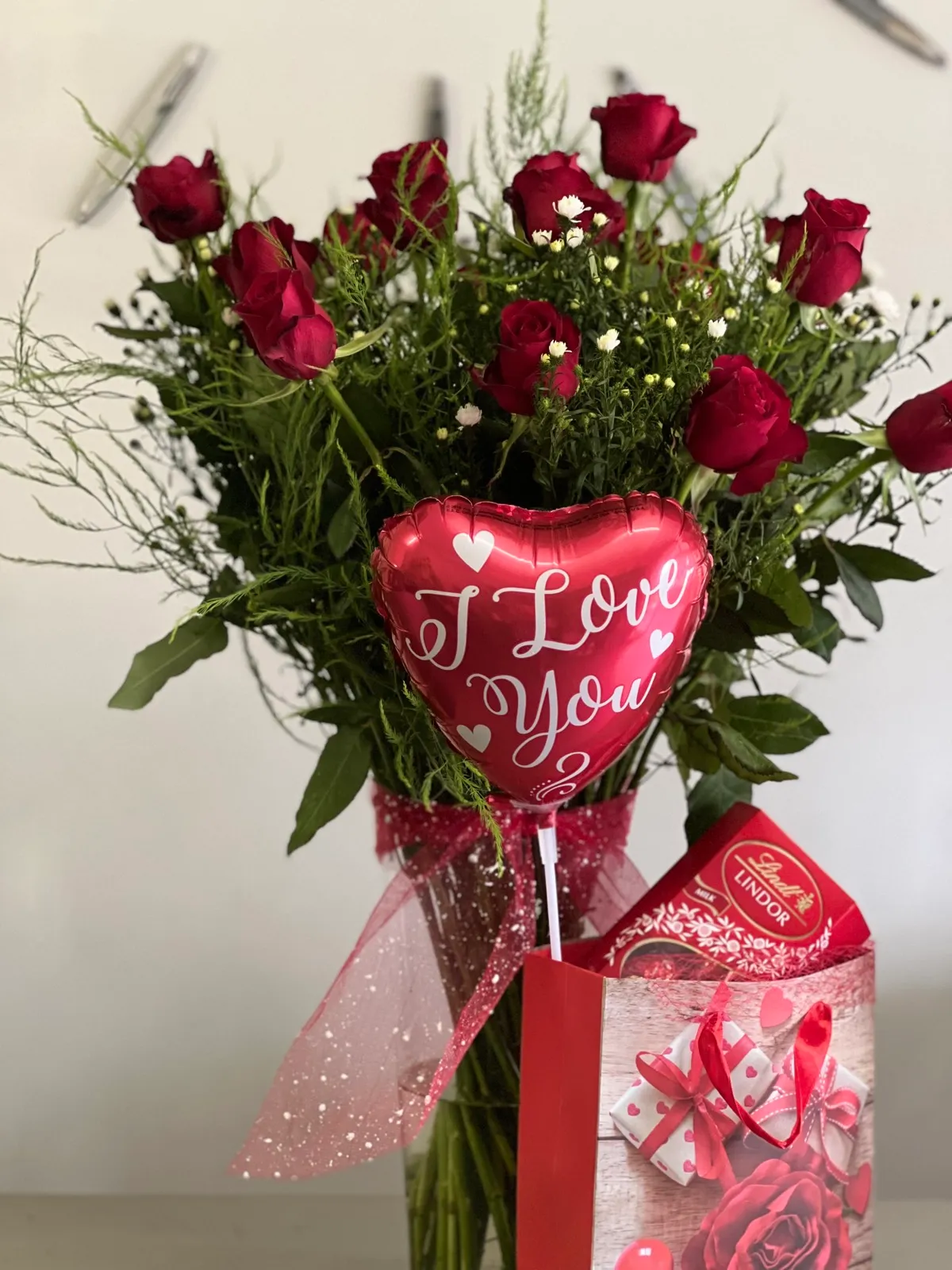 Red roses in a vase with an 'I Love You' balloon and a gift bag with Lindor chocolates