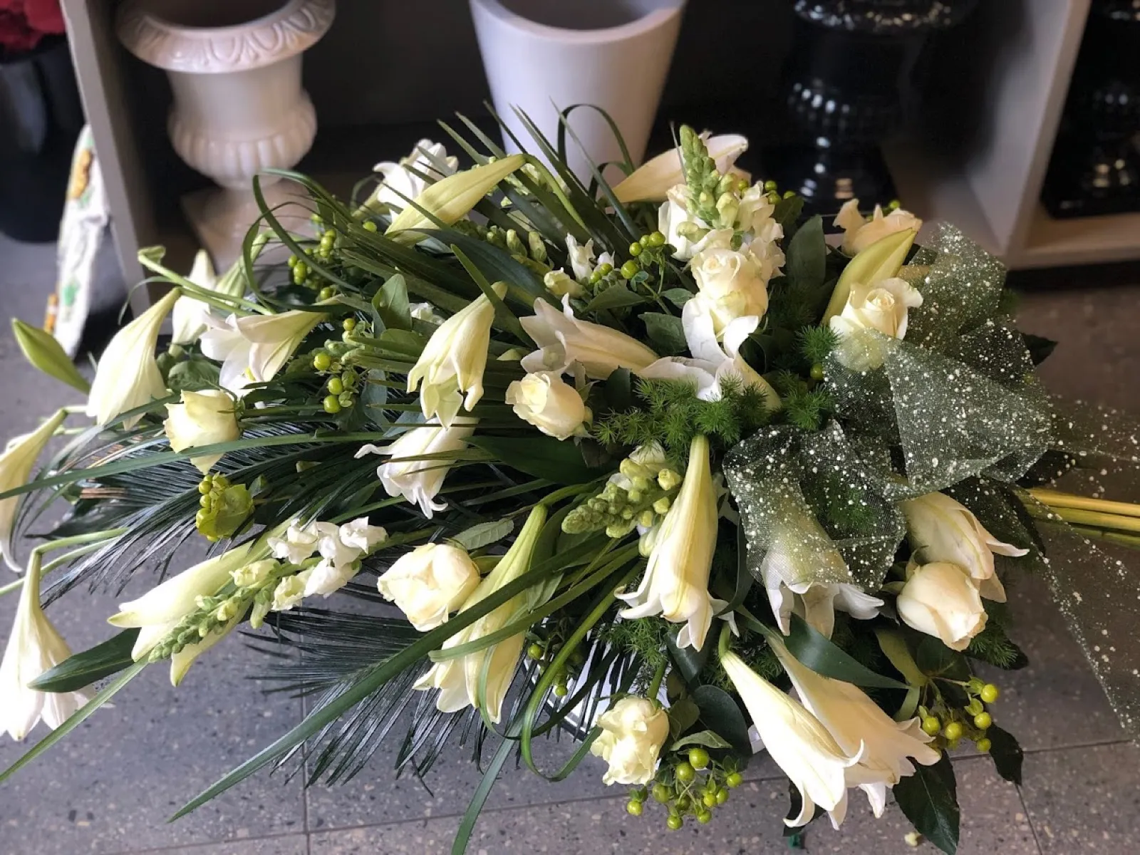 Hand-tied funeral sheath of white St Joseph lilies and roses with green berries