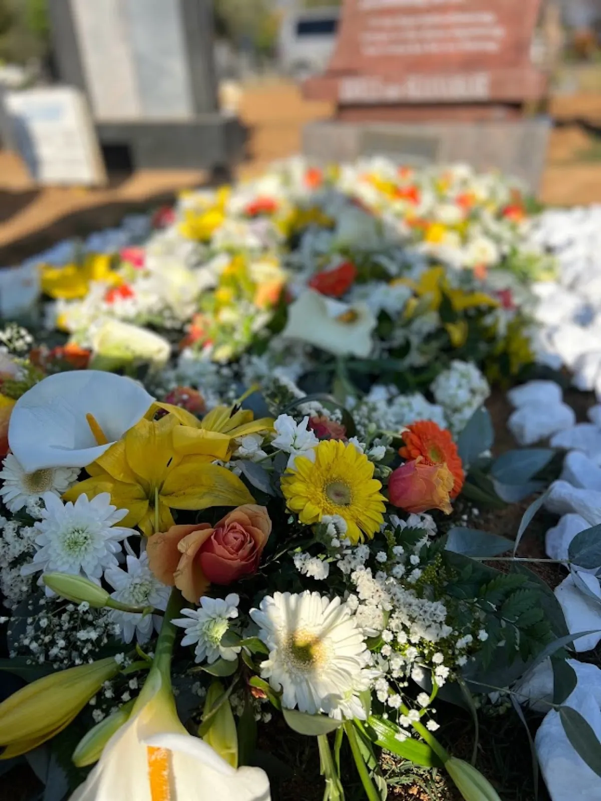 Grave fully covered in white, yellow and orange flowers for a tombstone unveiling