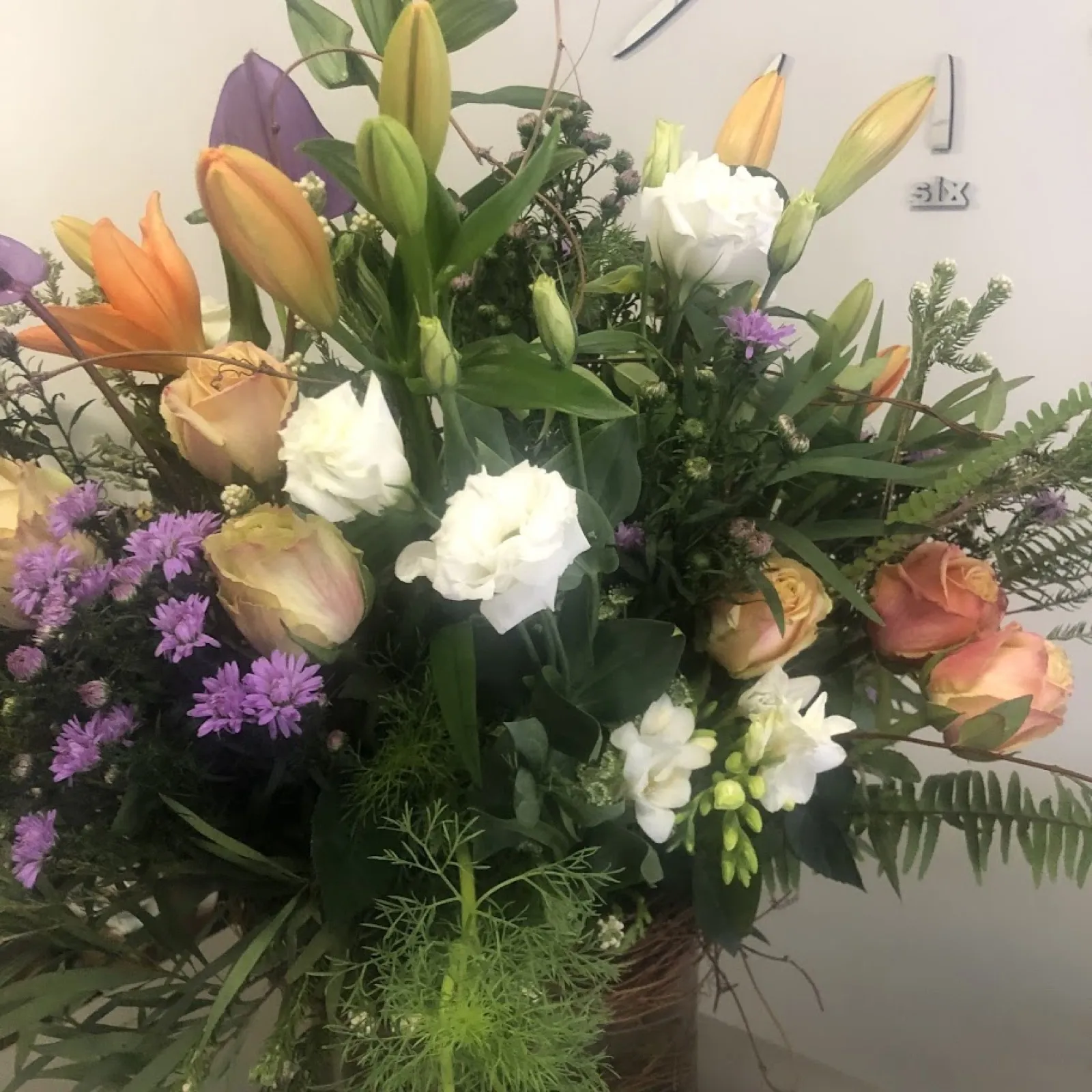 Free-style country arrangement of orange lilies, peach roses, white lisianthus and purple asters