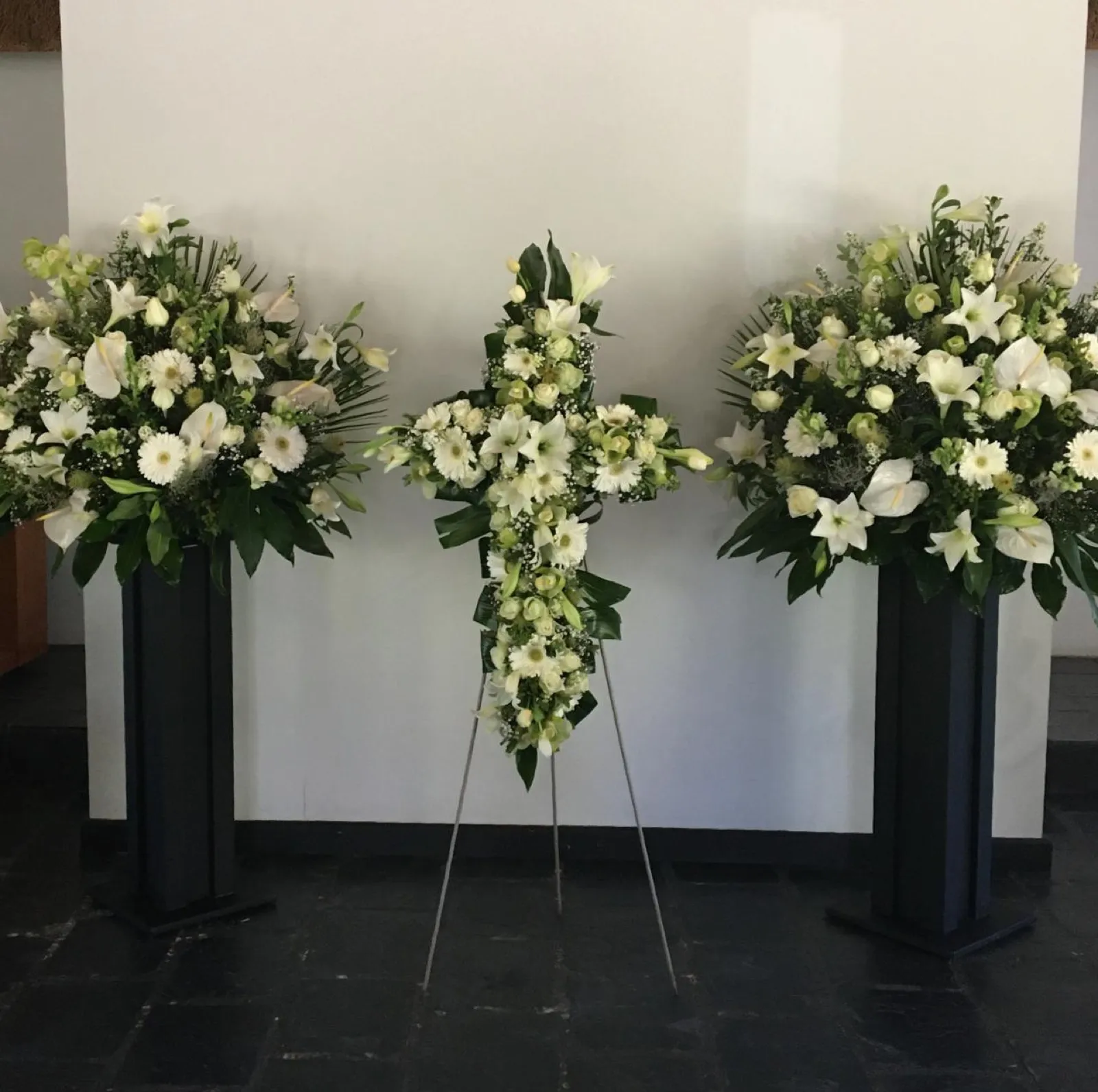 White flower cross on an easel between two white pedestal arrangements