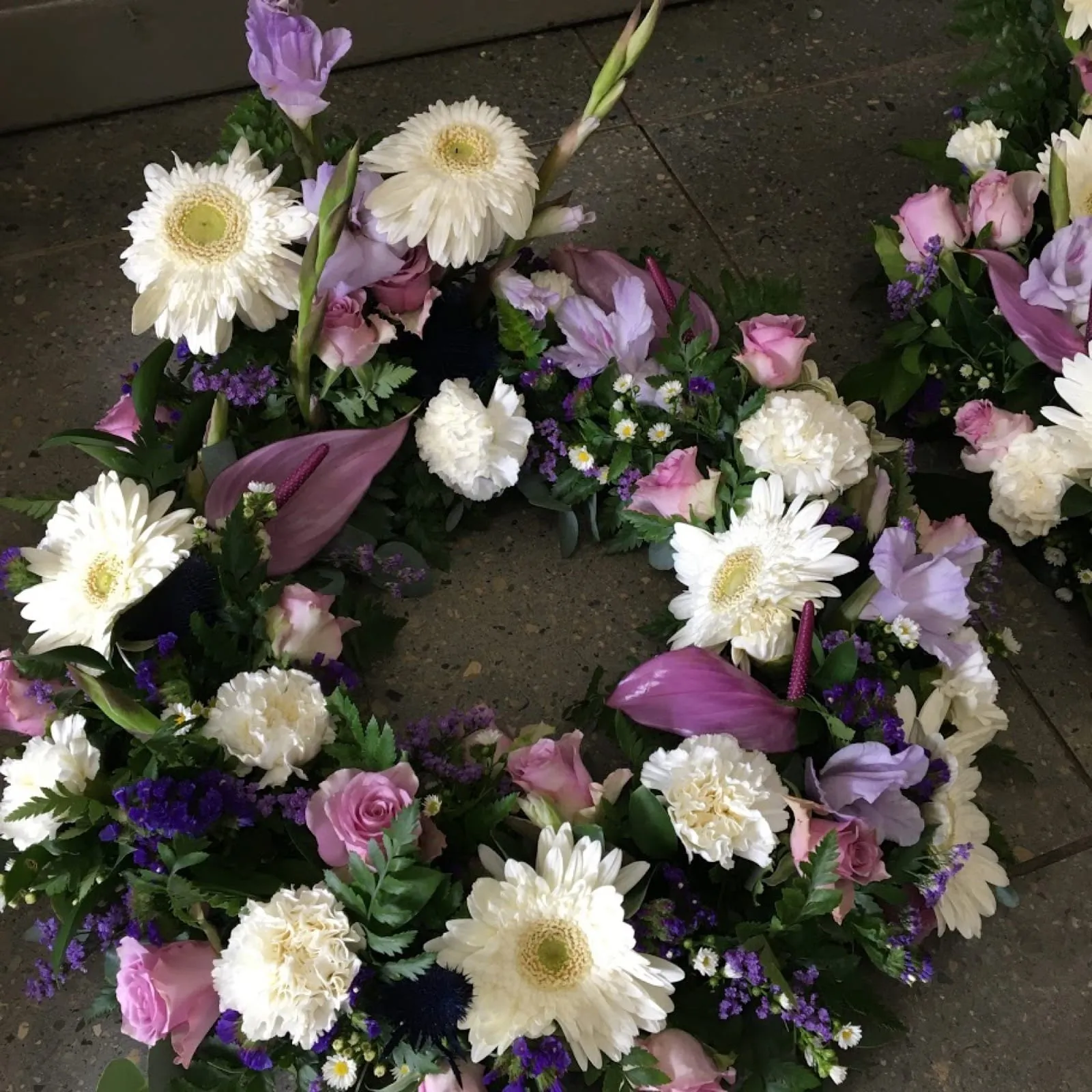 Round wreath of white gerberas and carnations with pink roses, lilac callas and purple statice